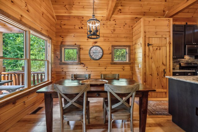 dining space featuring light wood-type flooring, wood walls, and lofted ceiling