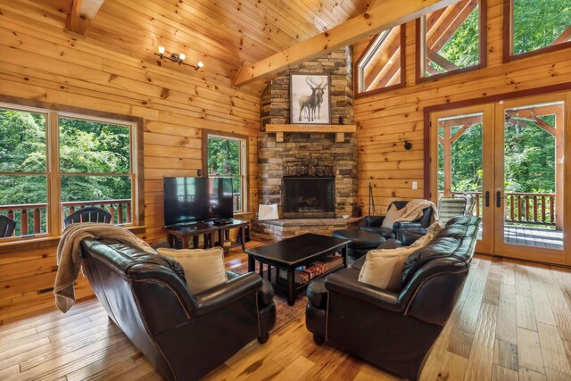 living room featuring high vaulted ceiling, a stone fireplace, beamed ceiling, light wood-type flooring, and french doors