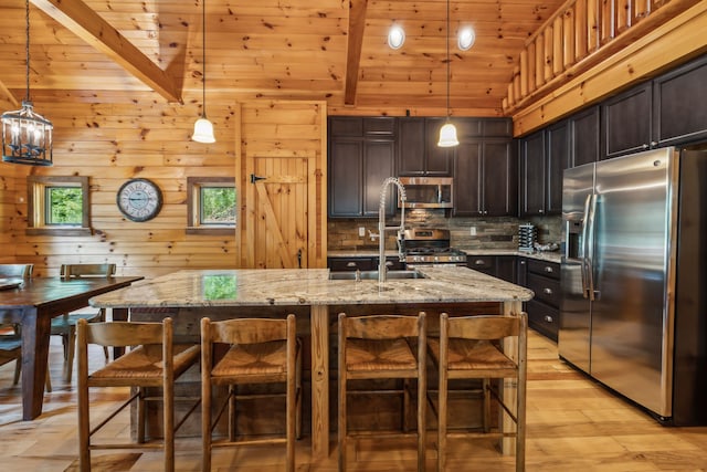 kitchen with hanging light fixtures, wood walls, light stone countertops, and stainless steel appliances