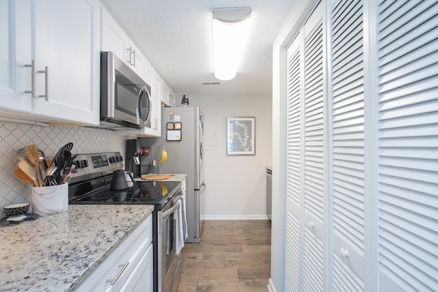 kitchen featuring appliances with stainless steel finishes, hardwood / wood-style floors, decorative backsplash, white cabinetry, and light stone countertops