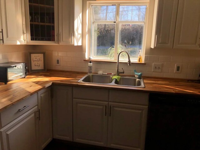 kitchen with decorative backsplash, sink, butcher block countertops, white cabinets, and black dishwasher