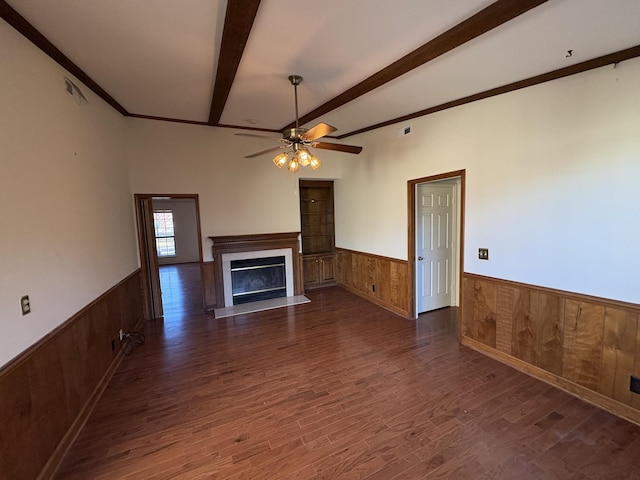 unfurnished living room featuring beam ceiling, ceiling fan, wooden walls, and dark hardwood / wood-style floors