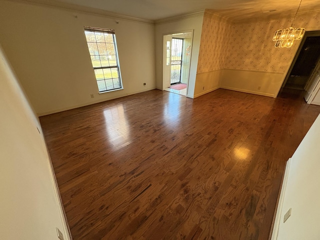 empty room featuring crown molding, dark hardwood / wood-style flooring, and a notable chandelier