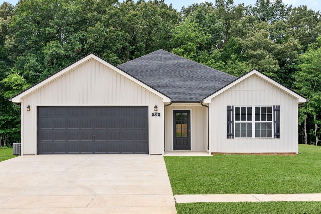 view of front of property featuring an attached garage, a shingled roof, concrete driveway, and a front yard