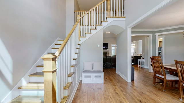 stairs with a towering ceiling, crown molding, and wood-type flooring