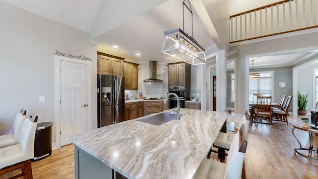 kitchen featuring light wood-style flooring, a sink, crown molding, wall chimney range hood, and stainless steel fridge