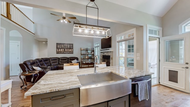 kitchen with gray cabinets, a stone fireplace, light hardwood / wood-style floors, light stone countertops, and dishwasher