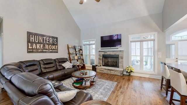 living area with a wealth of natural light, high vaulted ceiling, a stone fireplace, and wood finished floors