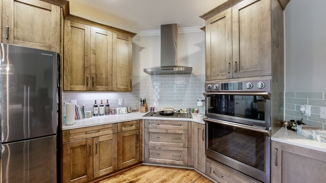 kitchen with light hardwood / wood-style floors, appliances with stainless steel finishes, wall chimney exhaust hood, and backsplash