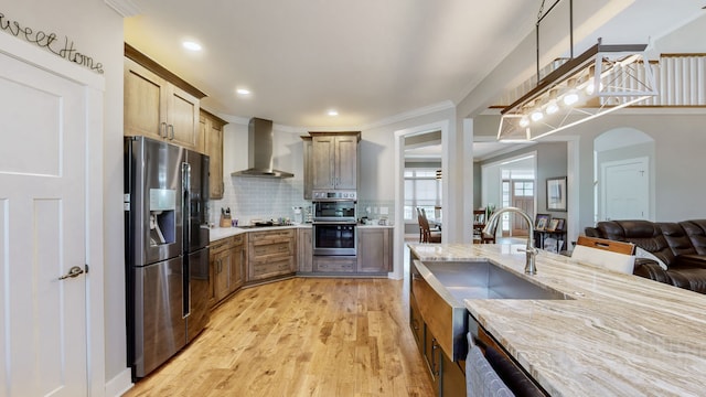 kitchen featuring backsplash, light wood-type flooring, wall chimney exhaust hood, light stone counters, and stainless steel appliances