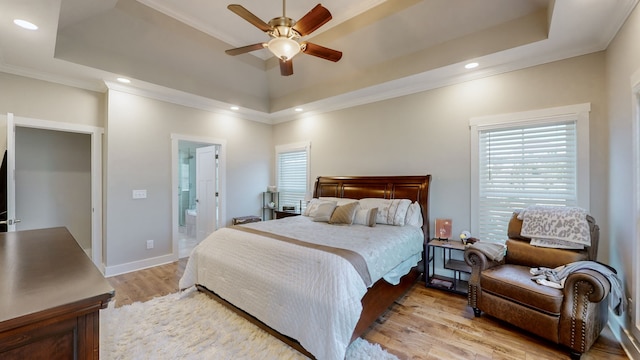 bedroom with ceiling fan, a raised ceiling, light hardwood / wood-style flooring, and ensuite bath