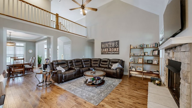 living room with ceiling fan, high vaulted ceiling, light hardwood / wood-style flooring, and a stone fireplace