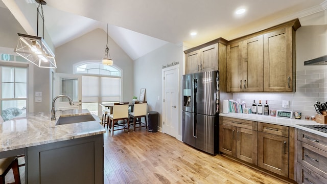 kitchen with decorative backsplash, sink, light stone counters, light wood-type flooring, and stainless steel fridge