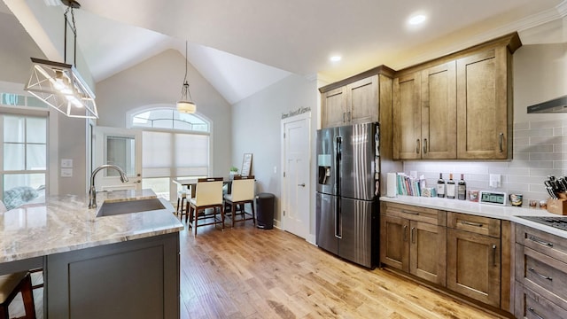 kitchen with vaulted ceiling, decorative backsplash, light wood-style flooring, stainless steel fridge, and a sink