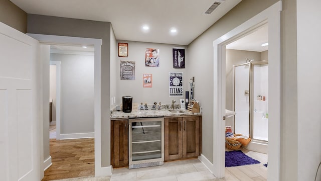 bar featuring beverage cooler, sink, light hardwood / wood-style flooring, and light stone counters