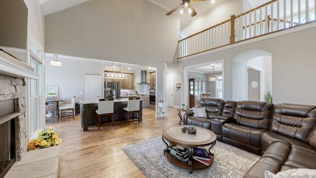 living room featuring light hardwood / wood-style floors, a towering ceiling, ceiling fan, and a fireplace