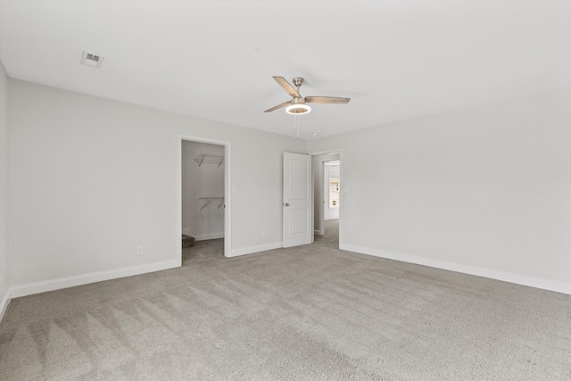 unfurnished bedroom with light colored carpet, ceiling fan, a walk in closet, and a closet