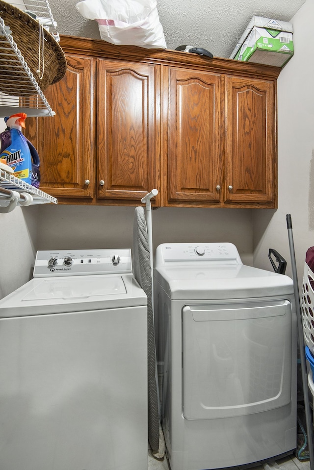 clothes washing area with a textured ceiling, washer and clothes dryer, and cabinets