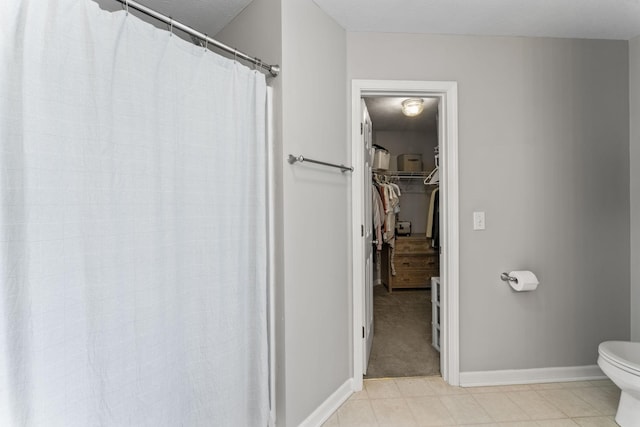 bathroom featuring a walk in closet, baseboards, and toilet