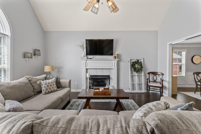 living room with ceiling fan, a tiled fireplace, dark wood-type flooring, and lofted ceiling