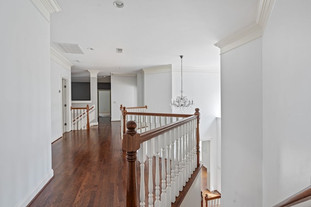 hallway featuring dark wood-type flooring, ornate columns, an inviting chandelier, and ornamental molding