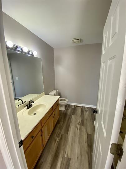 bathroom with visible vents, toilet, wood finished floors, baseboards, and vanity