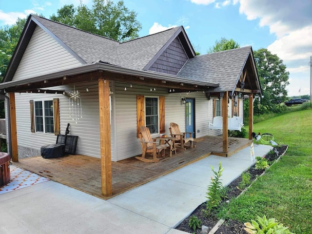 back of property with a porch, roof with shingles, and a lawn