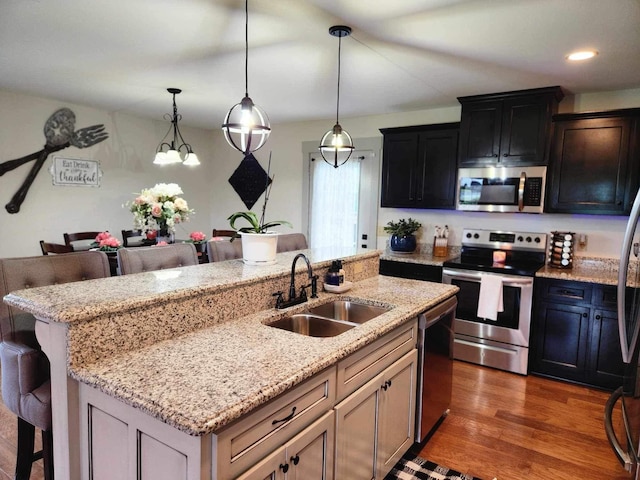 kitchen featuring a breakfast bar area, stainless steel appliances, a sink, an island with sink, and pendant lighting