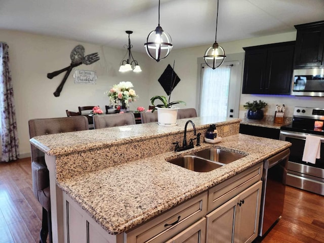 kitchen featuring stainless steel appliances, hanging light fixtures, dark wood-type flooring, a kitchen island with sink, and a sink