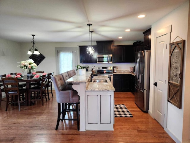 kitchen featuring a kitchen island with sink, appliances with stainless steel finishes, a breakfast bar area, and decorative light fixtures