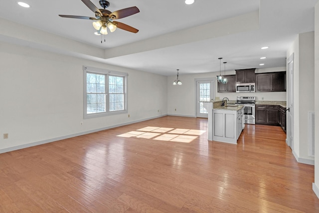 unfurnished living room featuring ceiling fan with notable chandelier, a wealth of natural light, and light hardwood / wood-style floors