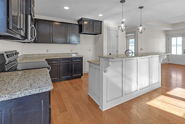 kitchen featuring decorative light fixtures, electric stove, a center island with sink, and light hardwood / wood-style floors