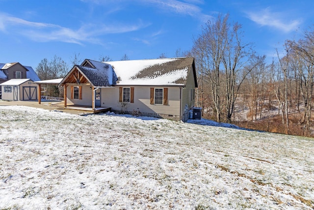 snow covered property with a deck, central AC unit, and a storage unit