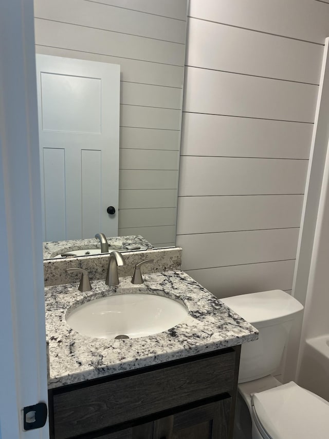 bathroom with wood walls, vanity, and toilet