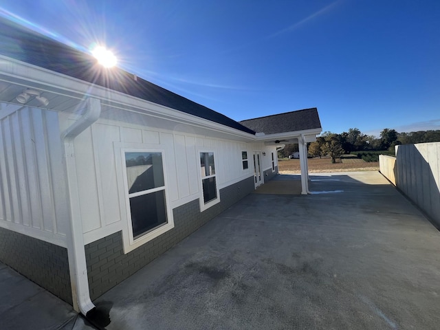 view of side of home featuring board and batten siding, a patio, fence, and brick siding