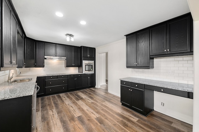 kitchen featuring backsplash, sink, stainless steel oven, hardwood / wood-style flooring, and light stone counters