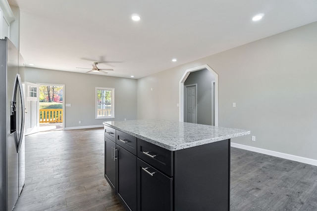 kitchen with dark wood-type flooring, stainless steel fridge, a center island, light stone counters, and ceiling fan