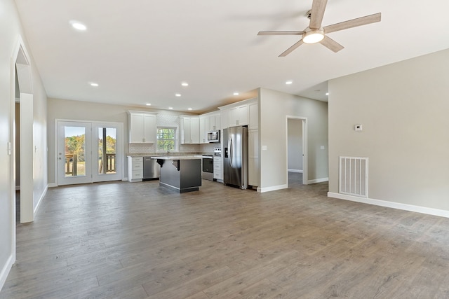 kitchen featuring a kitchen island, white cabinetry, stainless steel appliances, hardwood / wood-style flooring, and a breakfast bar area