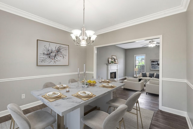 dining space with baseboards, a fireplace, dark wood-type flooring, crown molding, and ceiling fan with notable chandelier