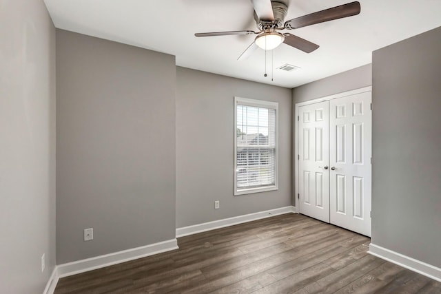 unfurnished bedroom with a closet, visible vents, dark wood-type flooring, and baseboards