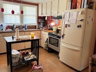 kitchen with under cabinet range hood, light wood-style floors, hanging light fixtures, freestanding refrigerator, and stainless steel range with electric stovetop