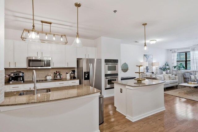 kitchen with appliances with stainless steel finishes, light hardwood / wood-style floors, sink, a center island, and hanging light fixtures