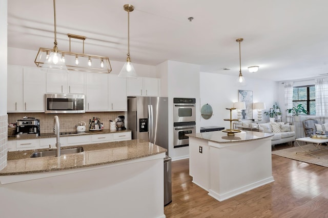 kitchen with hanging light fixtures, decorative backsplash, appliances with stainless steel finishes, white cabinetry, and a sink