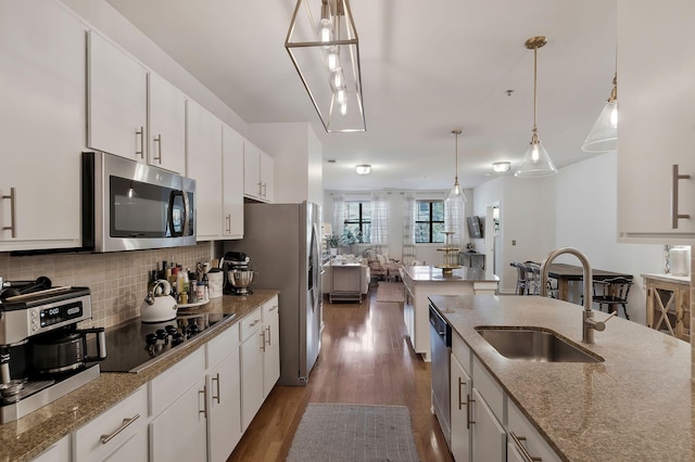 kitchen featuring appliances with stainless steel finishes, decorative light fixtures, light stone countertops, white cabinetry, and a sink