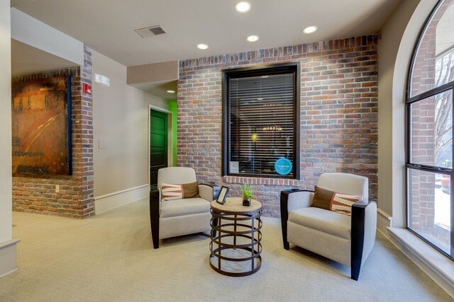 sitting room with brick wall and light colored carpet