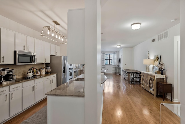 kitchen with light wood finished floors, stainless steel appliances, tasteful backsplash, visible vents, and white cabinets