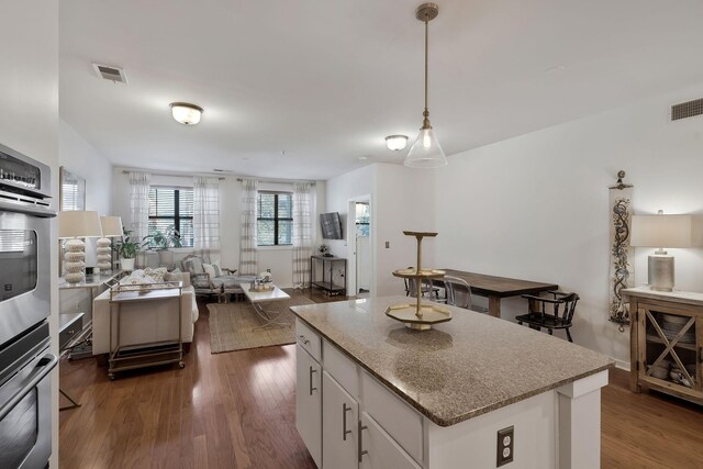 kitchen featuring double oven, wood-type flooring, a kitchen island, hanging light fixtures, and white cabinets