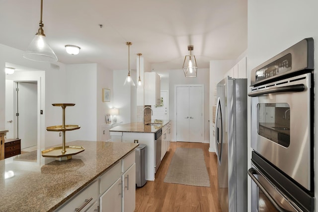 kitchen with stone countertops, appliances with stainless steel finishes, hanging light fixtures, light wood-style floors, and white cabinetry