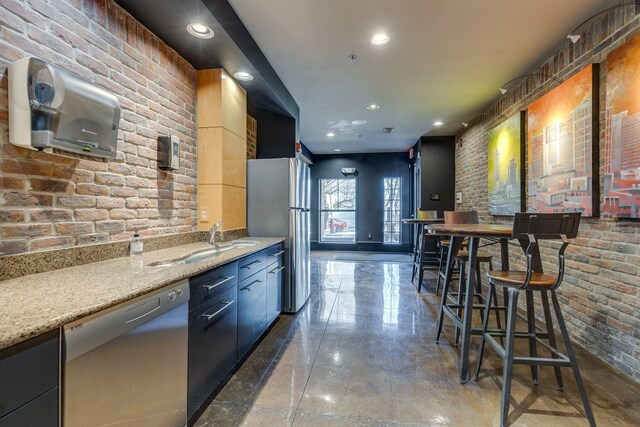 kitchen with sink, stainless steel appliances, brick wall, and light stone counters