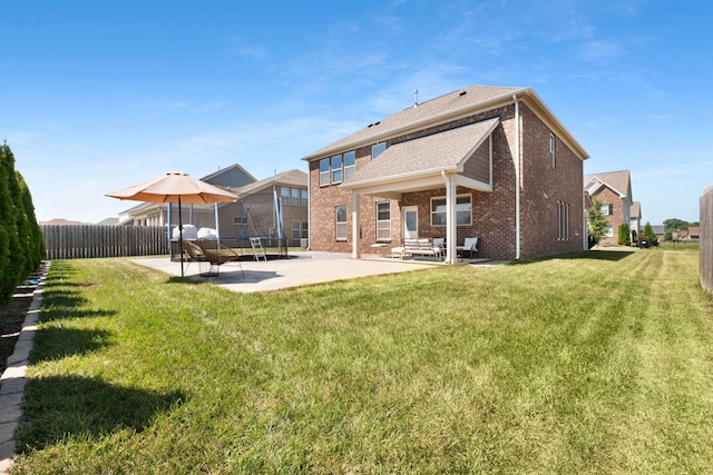 rear view of property with a trampoline, a patio area, and a yard